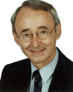A reversed enhanced colorized photographic headshot cutout of a glasses adorned smiling Peter A. Schouls wearing a light green shirt and dark blue tie under a dark blue jacket used to visually identify him.