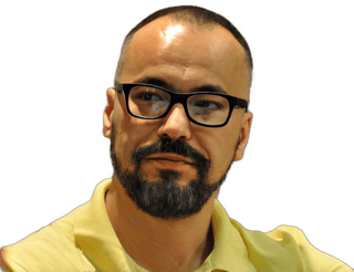An enhanced color photographic headshot cutout of Predrag Milidrag with black framed glasses and a brown mustache and trim beard with his head slightly turned to his right wearing a bright yellow polo shirt used to visually identify him.