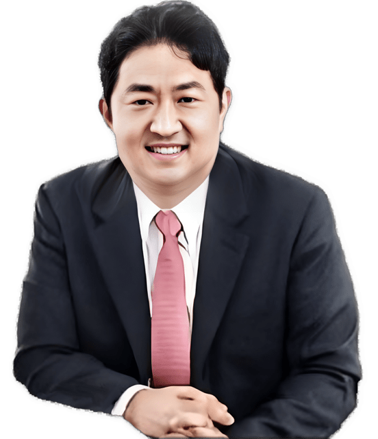 An enhanced color photographic headshot cutout from the waist up of a seated and  smiling Sukjae Lee wearing a black suit jacket, white collared shirt, and a pink colored tie used to visually identify him.