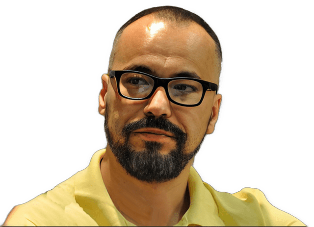 An enhanced color photographic headshot cutout of Predrag Milidrag with black framed glasses and a brown mustache and trim beard with his head slightly turned to his right wearing a bright yellow polo shirt used to visually identify him.