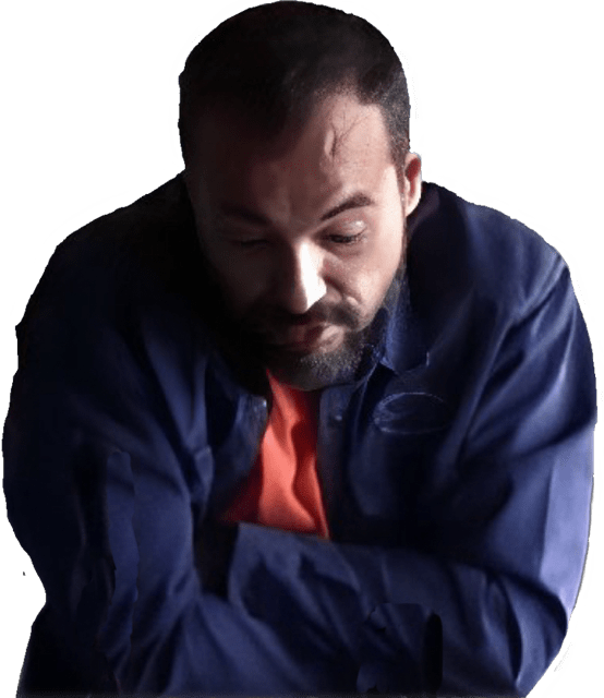 An enhanced color photographic torso and headshot cutout of Predrag Milidrag without glasses and a dark brown mustache and trim beard with his head slightly bent down and arms crossed wearing a purple-blue shirt and orange tie used to visually identify him.