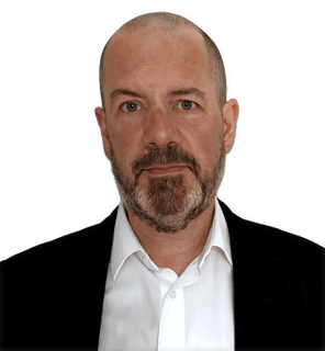 An enhanced colorized photographic shoulders and headshot of a full bearded and mustached Byron Williston with a salt and pepper colored beard and mustache and wearing a white collared shirt under a black suit coat used to visually identify him.