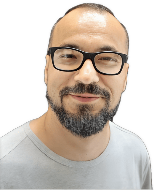 A reversed, enhanced color photographic headshot cutout of Predrag Milidrag, with a slight smile, black-framed glasses, and a brown mustache and beard, with his head looking straight forward, wearing a gray shirt with a rounded collar, is used to identify him visually.