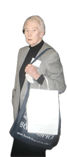 An enhanced color photographic cutout of a standing Annette C. Baier, wearing glasses and a black shirt under a gray jacket, carrying a large white bag over a large conference bag with writing on it, is used for visual identification.