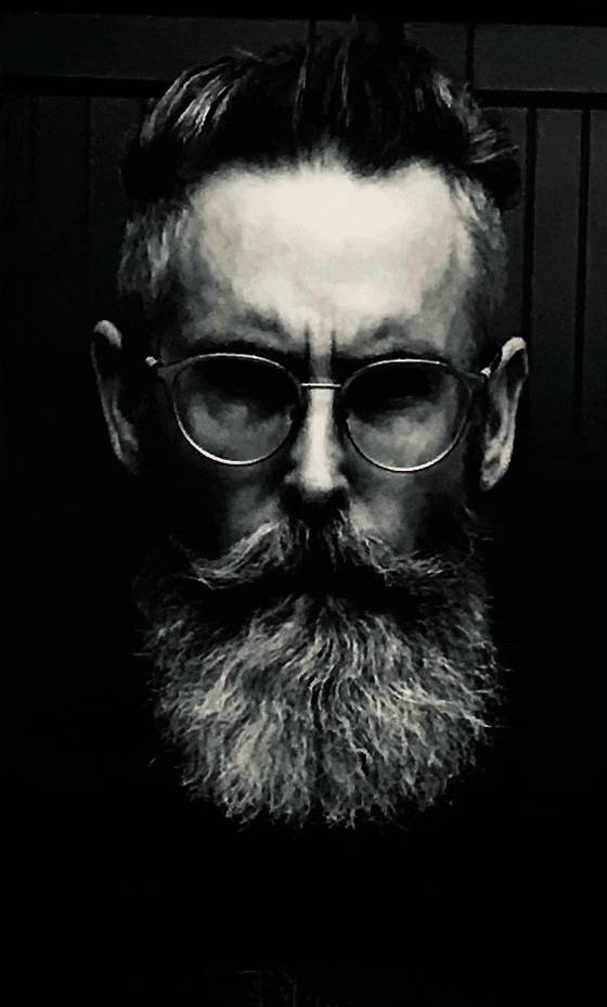 An animated .gif of Kurt Smith, starting in black and white and then shifting after an explosion of yellow into a colorized version of his head wearing glasses, a full gray beard, and a mustache with a stern look on his face, is used for visual identification.