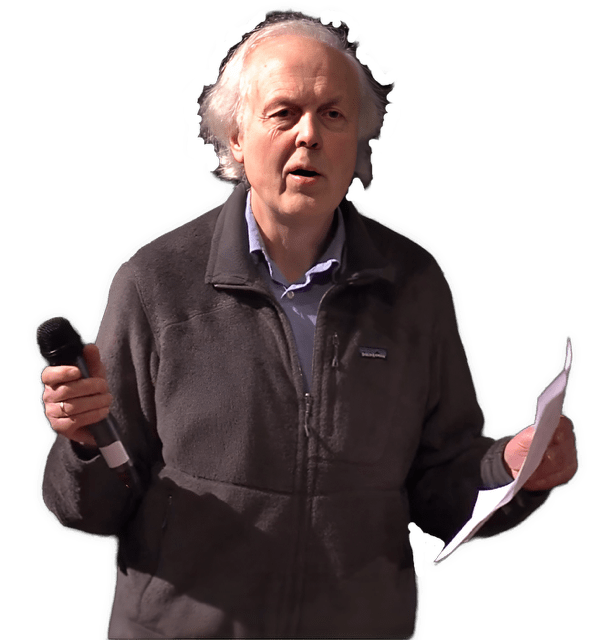 An enhanced color photographic upper torso and headshot cutout of Erwin Tegtmeier wearing a brown overcoat while holding a black wireless microphone in his right hand and lecture pages in his left hand are used for visual identification.