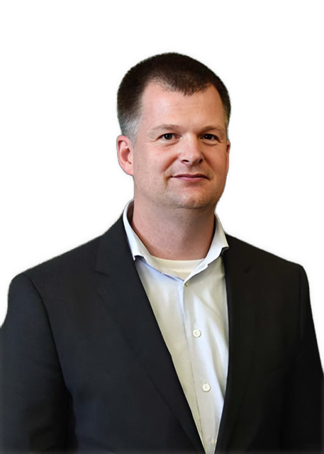 An enhanced photographic cutout of Johannes Haag from the waist up wearing an open-collar white shirt over a rounded-neck t-shirt under a black suit is used for visual identification.