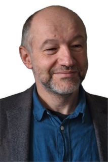 An enhanced colorized photographic headshot and upper chest cutout of a barely smiling slightly bearded Daniel Schmal wearing a blue shirt under a dark gray suit coat is used as a bullet point .